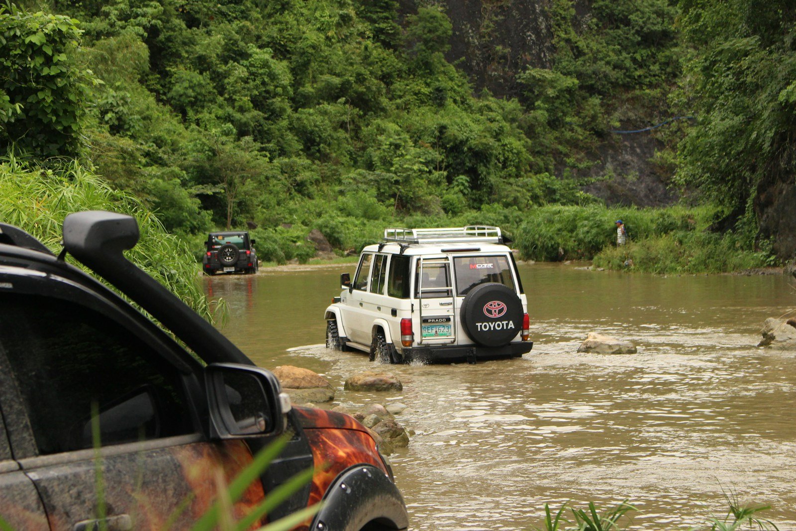 Off-road vehicles cross a flooded river.
